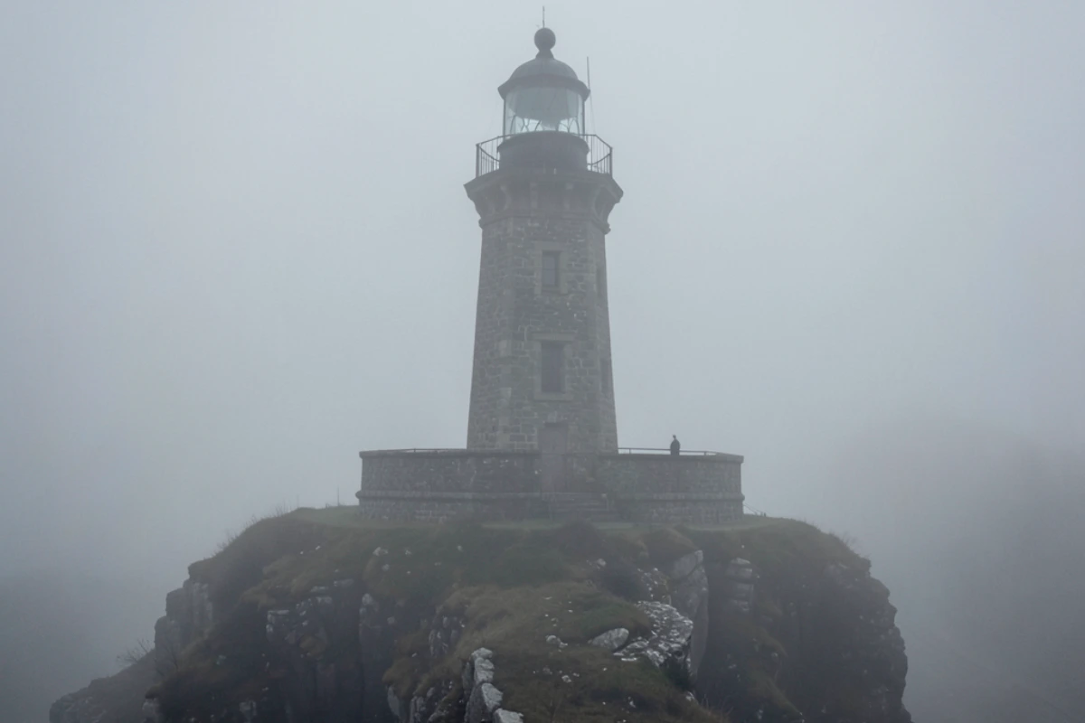 Un vecchio faro di pietra che svetta solitario sopra una scogliera durante una giornata di nebbia fitta. 