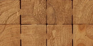 Dettaglio macro di blocchi di legno grezzo che si incastrano perfettamente tra loro, creando una struttura solida e simmetrica.