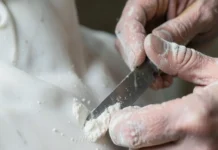 Inquadratura ravvicinata di mani esperte che usano uno scalpello per modellare una statua di marmo sotto una luce soffusa.