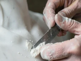 Inquadratura ravvicinata di mani esperte che usano uno scalpello per modellare una statua di marmo sotto una luce soffusa.