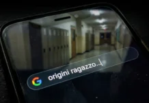 Smartphone in un ambiente oscuro con una ricerca Google sulle origini interrotta e un riflesso di un corridoio scolastico vuoto e sfocato.