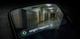 Smartphone in un ambiente oscuro con una ricerca Google sulle origini interrotta e un riflesso di un corridoio scolastico vuoto e sfocato.